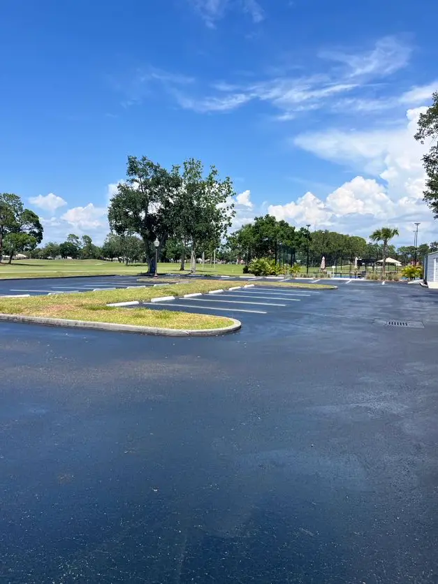 Freshly sealcoated commercial parking lot with crisp white striping lines at a golf course facility in Tampa, Florida. Jet-black sealcoat finish with clean white parking stall markings. Professional sealcoating and line striping by Radiant Striping, veteran-owned with 212 five-star Google reviews. Serving Tampa, St. Petersburg, Clearwater, and all of Tampa Bay. (813) 448-1252