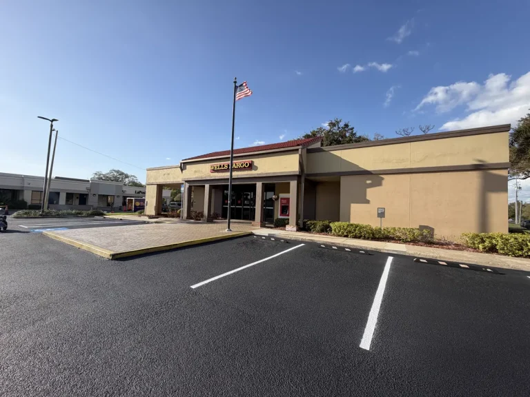 Freshly sealcoated commercial parking lot at Wells Fargo in Clearwater, Florida. Jet-black sealcoat with crisp white parking stall lines and blue ADA handicap markings. American flag visible. Professional sealcoating by Radiant Striping, veteran-owned with 212 five-star Google reviews. Serving Tampa, St. Petersburg, Clearwater, and all of Tampa Bay. (813) 448-1252.