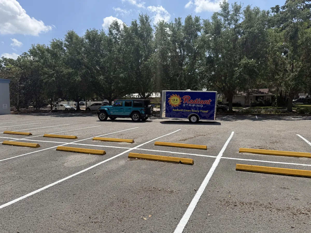 Fresh white parking stall lines and yellow wheel stops at a commercial lot in Brandon with the Radiant Striping trailer on site