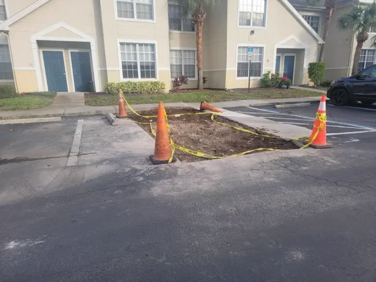 Asphalt repair in progress with excavated section and safety cones at Tampa apartment complex by Radiant Striping