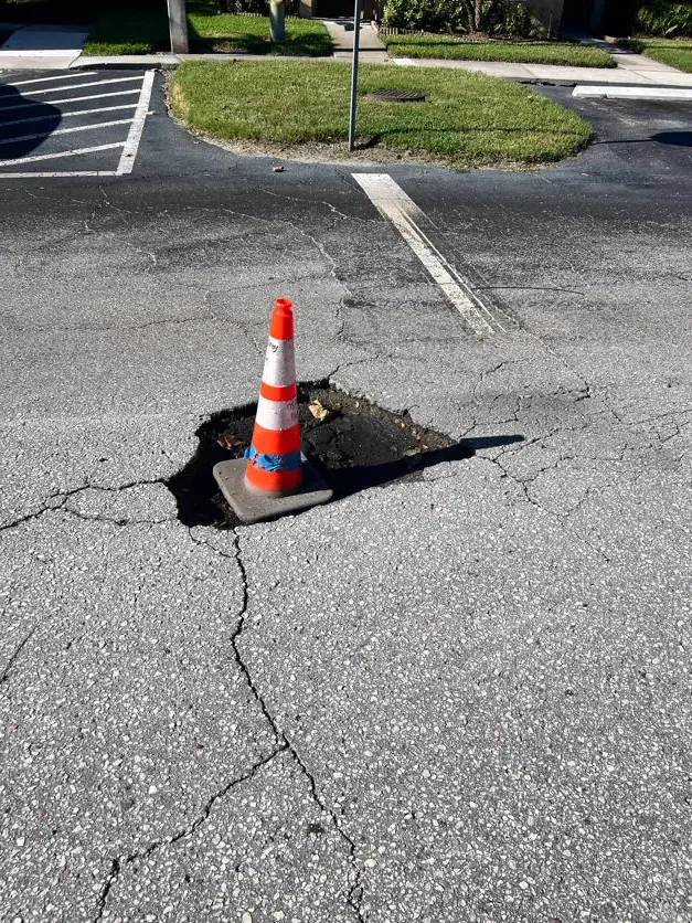 Deep pothole with traffic cone in damaged apartment parking lot before repair by Radiant Striping Tampa