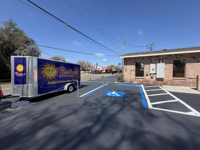 Radiant Striping branded trailer with sun logo in front of freshly completed commercial parking lot showing white stall lines blue ADA spaces and orange safety cones - commercial parking lot striping Tampa Florida
