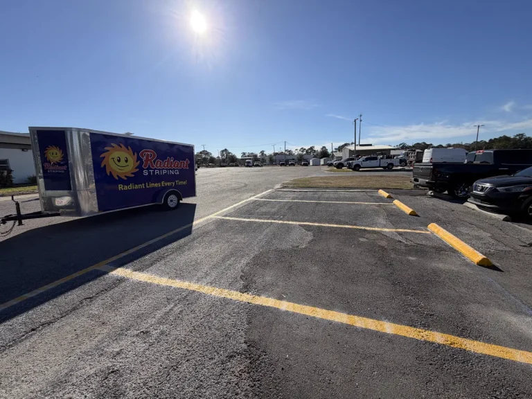 Radiant Striping branded trailer on job site with fresh yellow fire lane markings and safety bollards at commercial parking lot - fire lane striping by Radiant Striping Tampa Florida