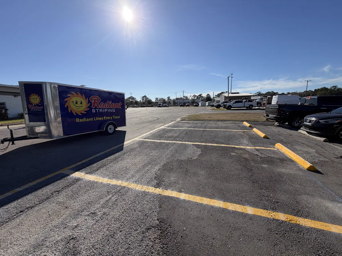 Radiant Striping branded trailer on job site with fresh yellow fire lane markings and safety bollards at commercial parking lot - fire lane striping by Radiant Striping Tampa Florida