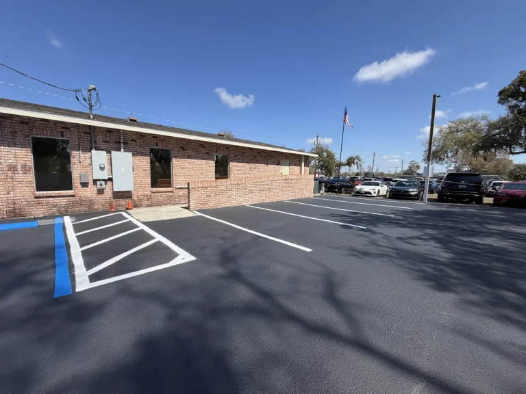 Freshly sealcoated and restriped commercial parking lot with crisp white stall lines and blue ADA handicap markings at brick office building - parking lot striping by Radiant Striping Tampa Florida